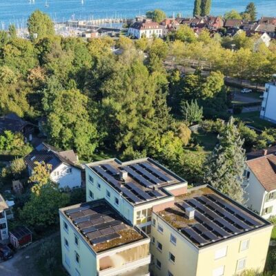 Blick von oben auf Ein- und Mehrfamilienhäusern mit PV-Anlagen in Ufernähe