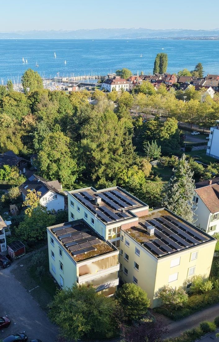 Blick von oben auf Ein- und Mehrfamilienhäusern mit PV-Anlagen in Ufernähe