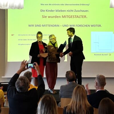 Zwei Vertreterinnen der Beethovenschule nehmen von Landrat Zeno Danner die Klimaschutzpreis-Urkunde und Trophäe entgegen
