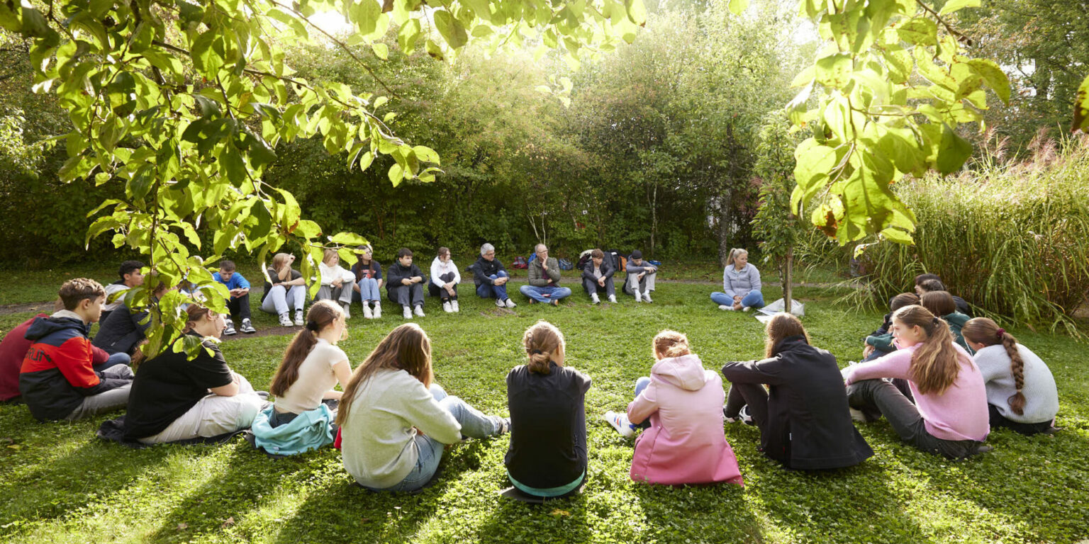 Schülerinnen und Schüler des Friedrich Wöhler Gymnasium Singen sitzen auf einer Wiese im Garten der Grünen Schule Mainau und diskutieren über Klimawandel